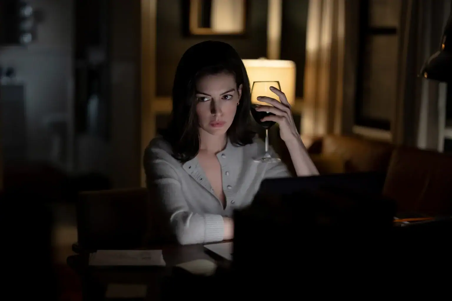 ‘Verity’ Review – A Twisty Thriller With Less Bite Than The Book A woman sits at a desk working on a laptop at night, holding a glass of red wine.