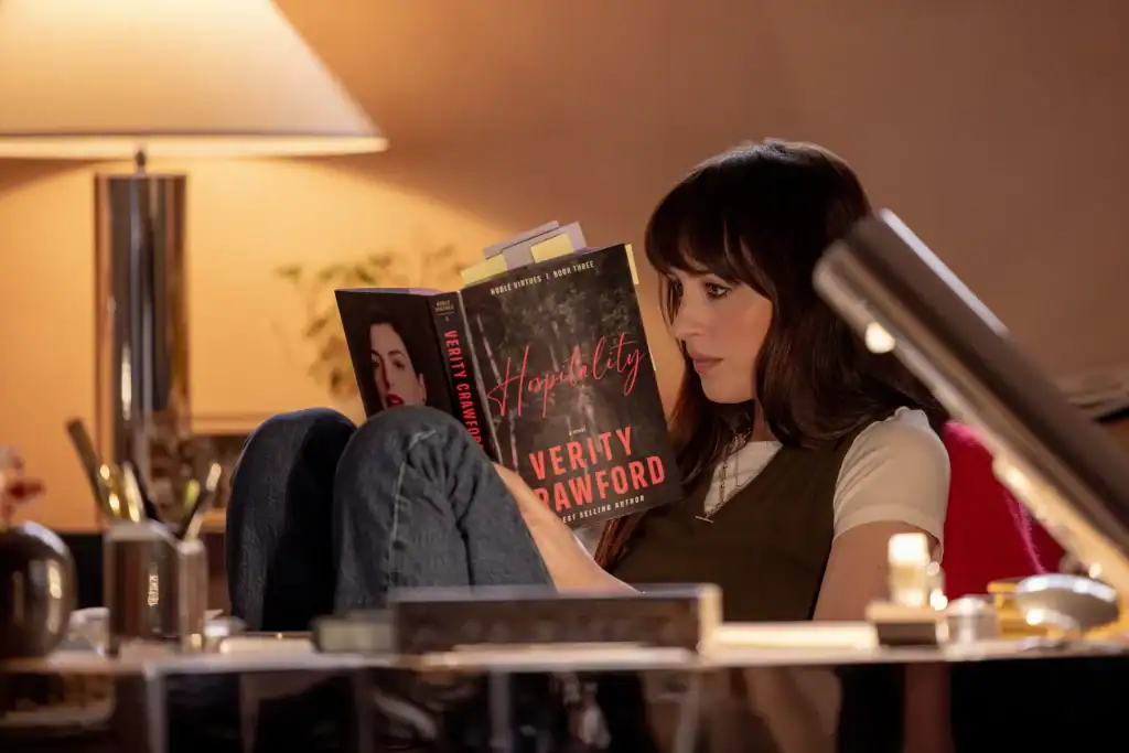 A woman sitting at a desk reads a book titled “Hospitality” by Verity Crawford.
